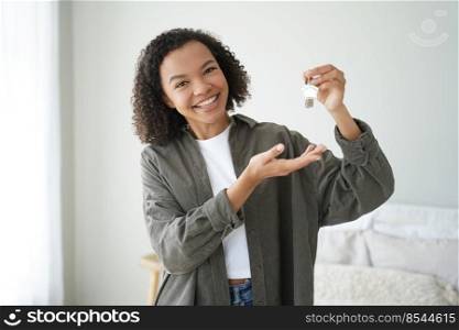 Happy biracial female buyer tenant of new home flat showing house keys. Young mixed race woman homeowner looking at camera demonstrates key of modern apartment. Mortgage, rental properties.. Happy biracial female buyer tenant of new home flat shows house keys. Mortgage, rental properties