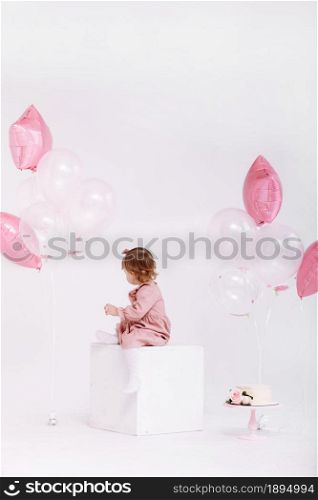 happy birthday 2 years old little girl in pink dress. white cake with candles and roses. Birthday decorations with white and pink color balloons and confetti for party on a white wall. Happy birthday.. happy birthday 2 years old little girl in pink dress. white cake with candles and roses. Birthday decorations with white and pink color balloons and confetti for party on a white wall. Happy birthday