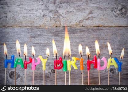 Happy birthday candles burn against wooden background
