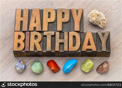 Happy Birthday greeting card in vintage letterpress wood type against grained wood with colorful polished stones and gypsum rosette