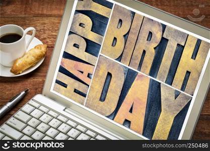 happy birthday greetings card in vintage letterpress wood type printing blocks on a laptop screen with a cup of coffee