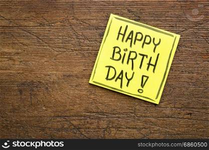 happy birthday greetings - handwriting in black ink on a sticky note against rustic wood