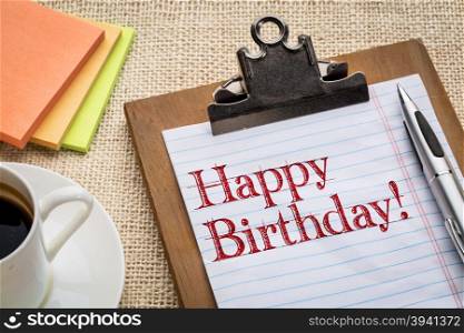 Happy Birthday on clipboard with a pen, coffee and sticky notes against burlap canvas - office celebration concept