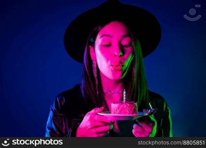 Happy birthday woman making wish - blowing candle on cake. Happy girl laughs, celebrating anniversary. Young stylish lady on blue background. High quality photo. Happy birthday woman making wish - blowing candle on cake. Happy girl laughs, celebrating anniversary. Young stylish lady on blue background.