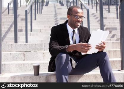happy black businessman sitting with coffee and documents handling
