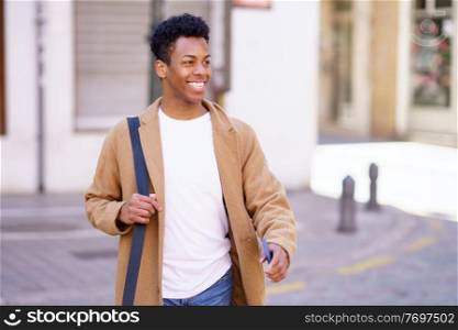 Happy black man walking down the street carrying a briefcase and a smartphone in his hand. Cuban guy smiling in urban background.. Happy black man walking down the street carrying a briefcase and a smartphone in his hand.