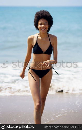 Happy black woman laughing while walking in bikini on the sand of the beach. Girl with afro hairstyle coming out of the water at the beach.. Happy black woman laughing while walking in bikini on the sand of the beach.