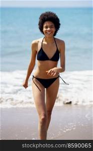 Happy black woman laughing while walking in bikini on the sand of the beach. Girl with afro hairstyle coming out of the water at the beach.. Happy black woman laughing while walking in bikini on the sand of the beach.