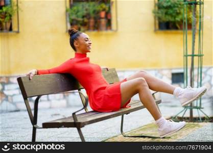 Happy black woman, waving her legs in joy, sitting on a bench in the street.. Happy mixed woman, waving her legs in joy, sitting on a bench in the street.