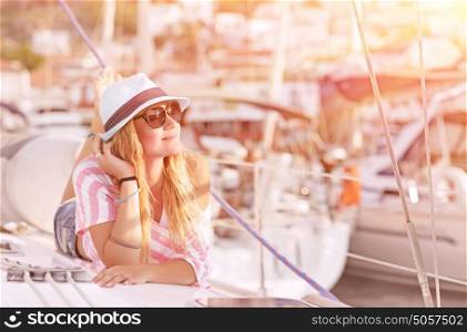 Happy blond female lying down on sailboat and enjoying beautiful sunset, summer adventure on luxury water transport, pleasure and relaxation concept