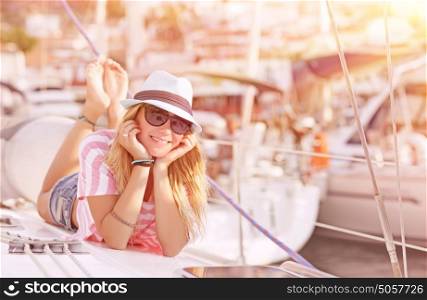 Happy blond female lying down on sailboat and enjoying beautiful sunset, summer adventure on luxury water transport, pleasure and relaxation concept