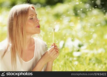 Happy blond Girl blow on dandelion in spring park