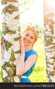 Happy blonde embracing birch trunk in the park