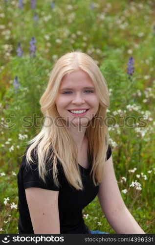 Happy blonde girl in the field surrounded by flowers