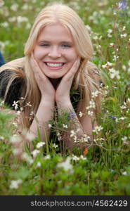 Happy blonde girl in the field surrounded by flowers