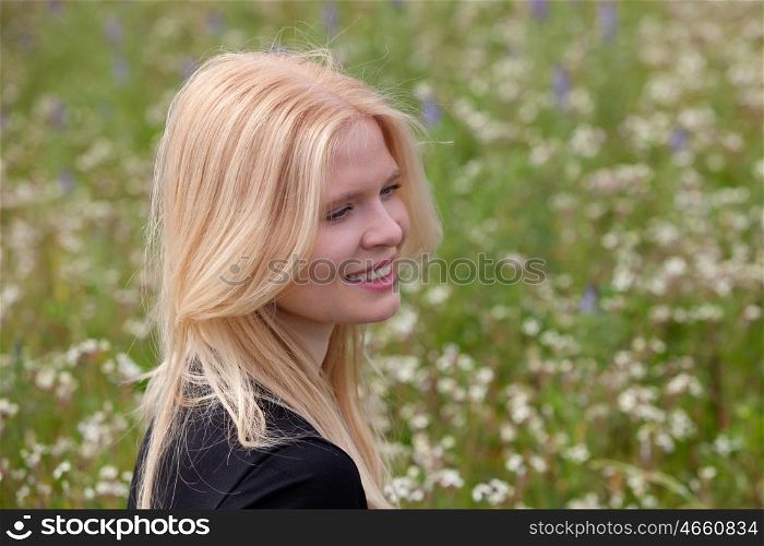 Happy blonde girl in the field surrounded by flowers