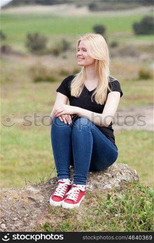 Happy blonde girl outside sitting on a big stone