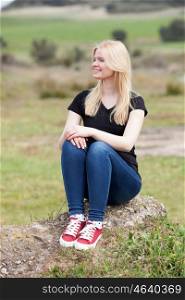 Happy blonde girl outside sitting on a big stone