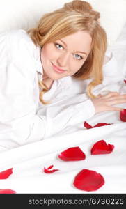 happy blonde woman in bed with red rose petals