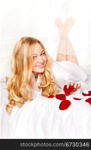 happy blonde woman in bed with red rose petals
