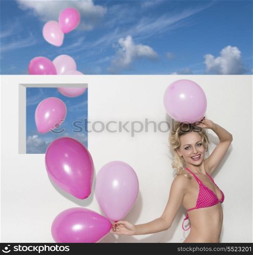 happy blonde woman wearing sexy pink bikini and playing with balloons. Smiling in summertime