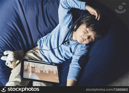 Happy boy lying on bean bag closing his listening music from digital tablet, Positive boy staying at home relaxing after online homework lesson from school during quarantine.Distance education, E-learning and Self Distancing