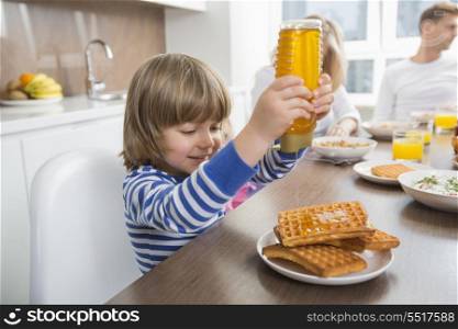 Happy boy pouring honey on waffles while having breakfast with family