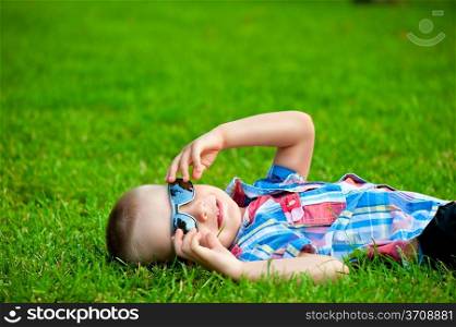 happy boy resting lying on green grass in sunglasses