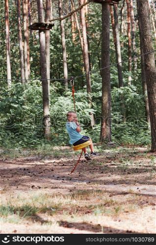 Happy boy riding on the zip line in rope park in forest while spending summer vacation. Real people, authentic situations