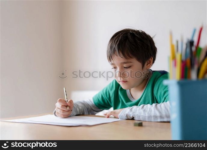 Happy boy using pencil drawing or sketching on paper, Portrait kid siting on table doing homework, Child enjoy art and craft activity at home, Education concept