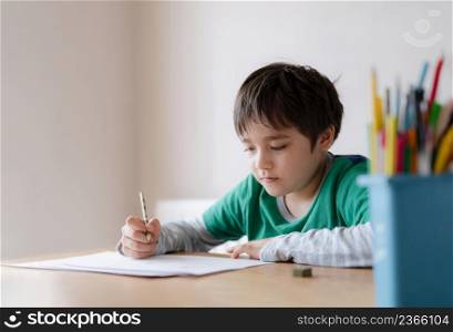 Happy boy using pencil drawing or sketching on paper, Portrait kid siting on table doing homework, Child enjoy art and craft activity at home, Education concept