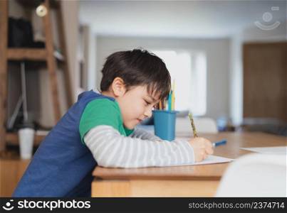 Happy boy using pencil drawing or sketching on paper,Portrait  kid siting on table doing homework in living room,Child enjoy art and craft activity at home on weekend,Education, Home schooling concept