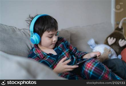 Happy boy wearing headphone listening to music, Kid with smiling face having fun playing game online on tablet with friends on holiday, Child wearing pajamas relaxing at home in the morning