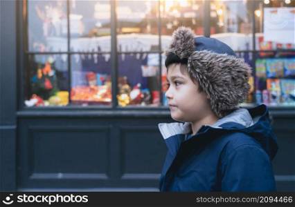 Happy boy with fluffy hat and warm jacket walking outside in the city, Cute kid with funny face standing outside with blurry street background,Child having fun playing in old town on Christmas holiday