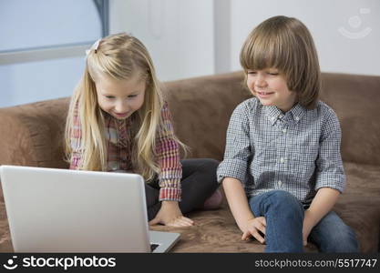 Happy boy with sister using laptop on sofa