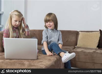 Happy boy with sister using laptop on sofa