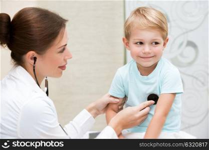Happy brave little boy at the doctor, young female pediatrician using stethoscope listening babys lungs, enjoying visits to doctor