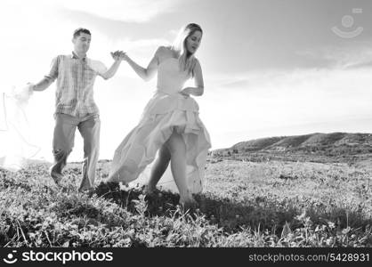 happy bride and groom walking and run on beautiful meadow outdoor at sunset