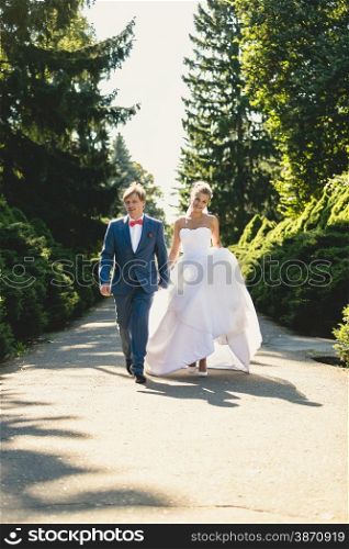 Happy bride and groom walking at summer park at sunny day