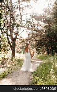 happy bride girl in a white light dress with a bouquet of dried flowers on a forest path
