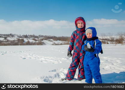 Happy brother and sister play on a winter walk, making snowballs in the park. Winter outdoor games. The winter vacation. Happy childhood.. Happy brother and sister play on a winter walk, making snowballs in the park. Winter outdoor games.