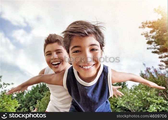 Happy brothers having fun outdoors, playing as if flying, two active boys spending summer holidays with pleasure in a countryside