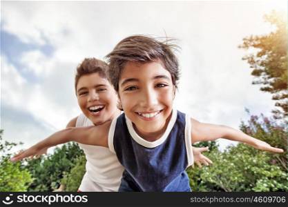 Happy brothers having fun outdoors, playing as if flying, two active boys spending summer holidays with pleasure in a countryside