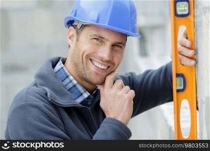 happy builder posing with spirit level at construction site