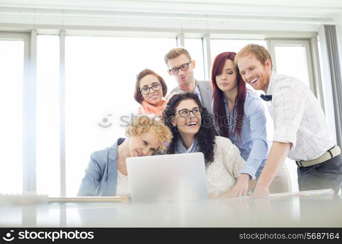 Happy business colleagues with laptop discussing in creative office