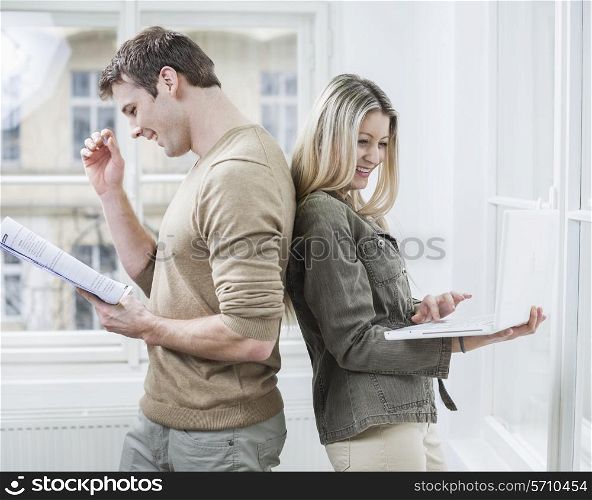 Happy business couple holding book and laptop in office