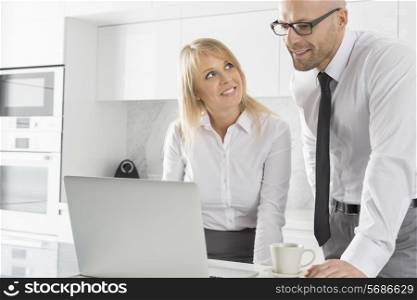 Happy business couple working on laptop in kitchen
