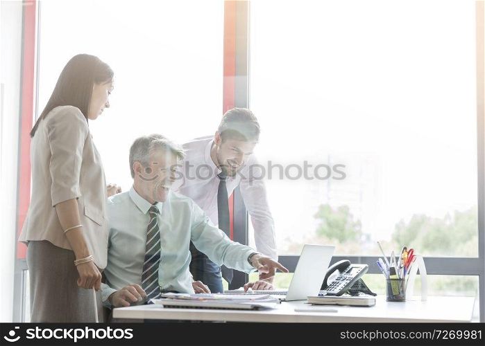 Happy business people looking at laptop seen through window in office