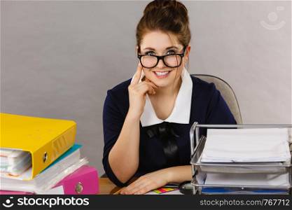 Happy business woman feeling energetic sitting working at desk full off documents in binders.. Happy business woman in office