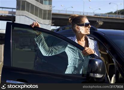 happy business woman in sunglasses near the car against city bridge